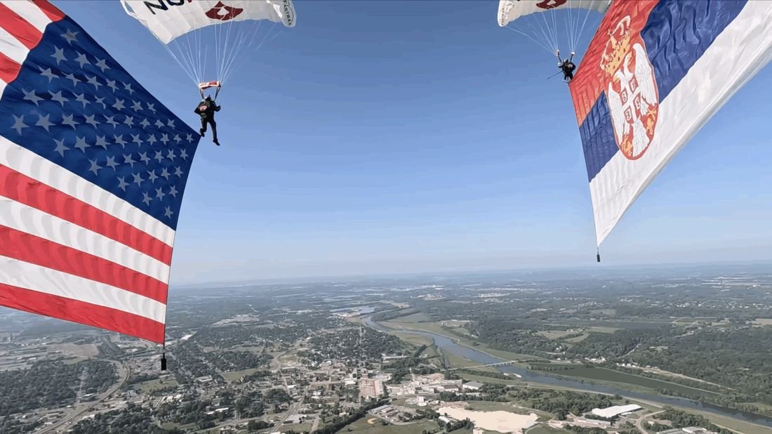 American and Serbian flags flying under parachutes